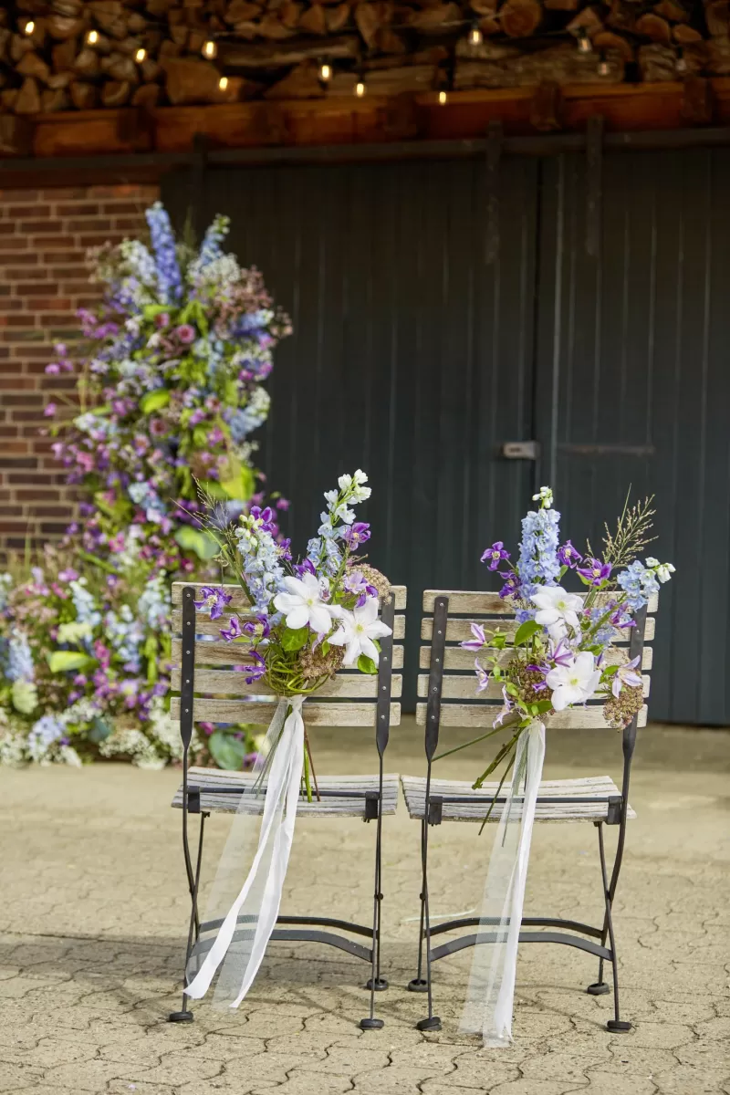 Bruiloft stoelen ceremonie trouwbloemen Clematis Amazing® ‘Oslo’, ‘Star River’, ‘Vienna’, Daucus Carota ‘Dara’, Delphinium ‘Guardian Lavender’, Miscanthus ‘White Cloud’